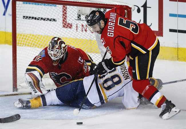 Nashville Predators' Viktor Arvidsson, centre, from Sweden, crashes into Calgary Flames goalie Chad Johnson, left, as Mark Giordano grabs a loose puck during first period NHL hockey action in Calgary, Thursday, Jan. 19, 2017.