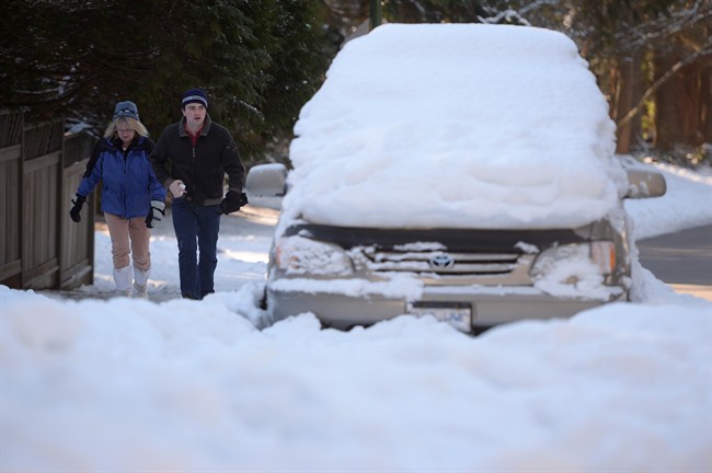 People make their way past a snow-covered vehicle on a street in Vancouver, Wednesday, Jan.4, 2017.