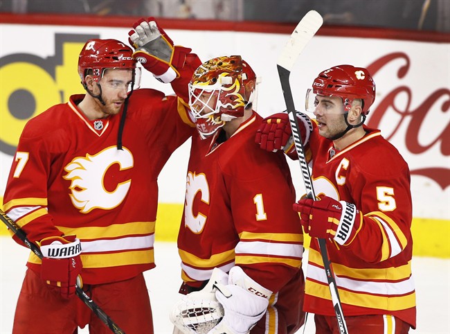 Calgary Flames' goalie Brian Elliott, centre, is congratulated by TJ Brodie, left, and Mark Giordano on a 4-2 victory over the Arizona Coyotes after NHL action in Calgary, Alta., Sat., Dec. 31, 2016.