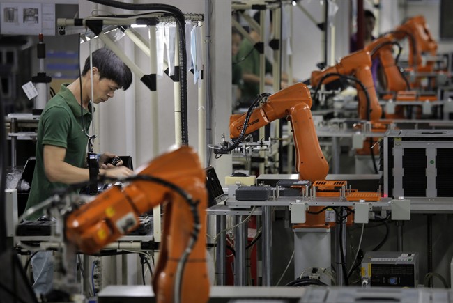In this Aug. 21, 2015 photo, a man works amid orange robot arms at Rapoo Technology factory in southern Chinese industrial boomtown of Shenzhen. 