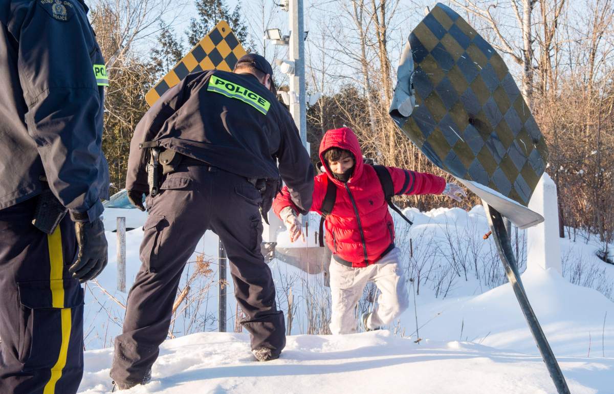 An RCMP officer extends his hand to help a young man from Yemen to cross into Canada at the U.S.-Canada border into Canada near Hemmingford, Que., on Friday, Feb. 17, 2017. A number of refugee claimants are braving the elements to illicitly enter Canada.