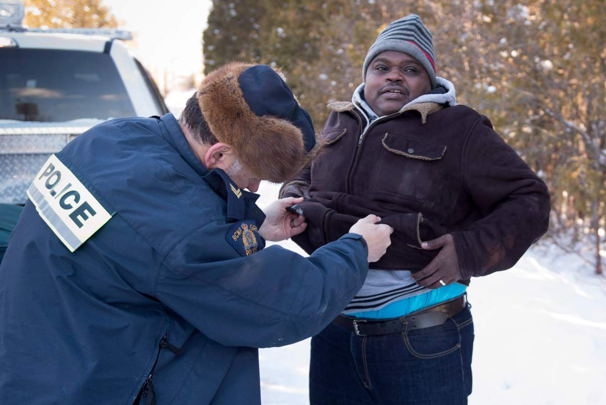 A Somali man is frisked by an RCMP officer after crossing the U.S.-Canada border into Canada near Hemmingford, Que., on Friday, Feb. 17, 2017. A number of refugee claimants are braving the elements to illicitly enter Canada.