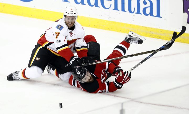 Calgary Flames defenseman TJ Brodie (7) pins down New Jersey Devils right wing Kyle Palmieri (21) while hitting the ice during the pursuit of the puck in the third period of an NHL hockey game, Friday, Feb. 3, 2017, in Newark, N.J. 