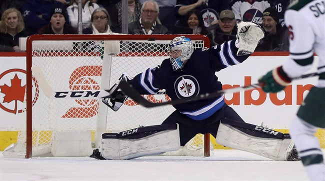 Winnipeg Jets goalie Connor Hellebuyck stretches to make a save as the puck hits the crossbar on a shot by the Minnesota Wild during an NHL hockey game in Winnipeg on February 7, 2017.
