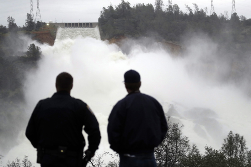 Two men watch as water gushes from the Oroville Dam’s main spillway Wednesday, in Oroville, Calif.