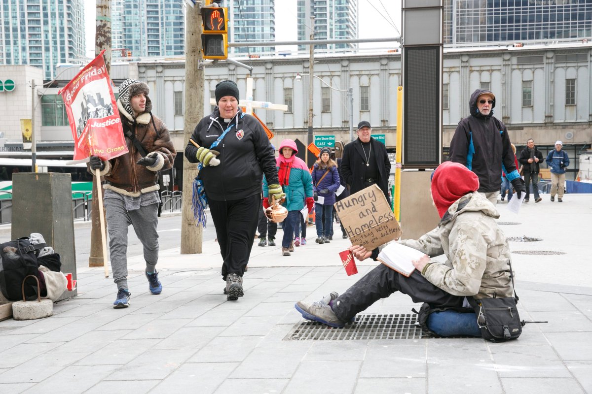 Marchers participating in a Good Friday "justice march" walk past a man panhandling on the sidewalk at an intersection in downtown Toronto on Friday, March 25, 2016. THE CANADIAN PRESS IMAGES/Michael Hudson.