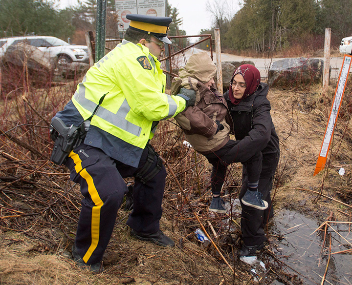 An RCMP officer helps asylum seekers, claiming to be from Turkey, cross the border from New York into Canada on Wednesday, March 8, 2017 in Hemmingford, Quebec. 