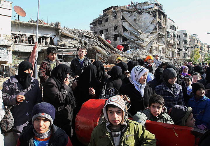 This Wednesday, Jan. 14, 2015 file photo, shows Syrians amid rubble as they wait in line at a military checkpoint in the town of Beit Sahm, south of the capital, Damascus. 