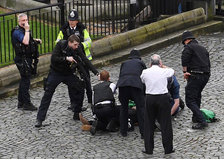 A policeman points a gun at a man on the ground as emergency services attend the scene outside the Palace of Westminster, London.