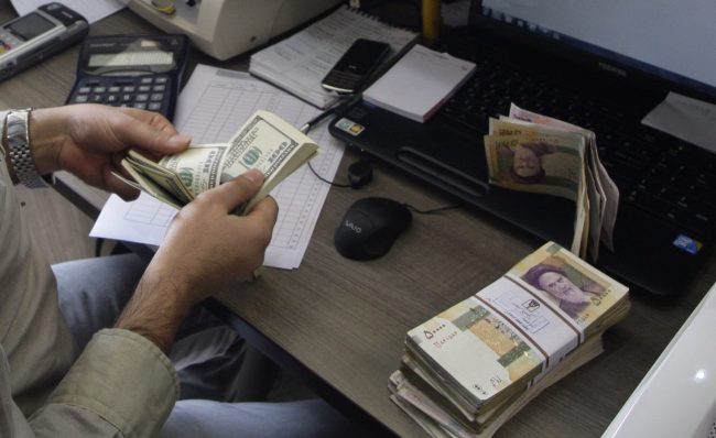 A currency exchange bureau worker counts US dollars, as Iranian bank notes are seen at right, in downtown Tehran, Iran, in this Wednesday, Dec. 21, 2011 file photo. 