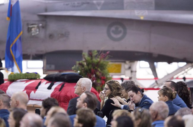 Caitlin Skelhorn, the fiancee of Capt. Thomas McQueen, wipes away tears while she sits with his parents watching a tribute video during the funeral service for Canadian Air Force pilot McQueen at the Warplane Heritage Museum in Hamilton, Ont., December 7, 2016. Capt. McQueen died when the CF-18 he was piloting crashed during a training mission at CFB Cold Lake on Nov. 27, 2016. 