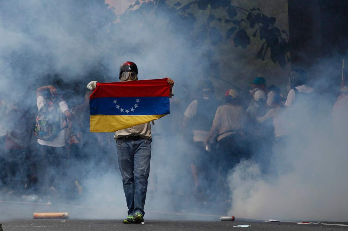 An anti-government protester holds a Venezuelan flag during clashes against security forces in Caracas, Venezuela, Wednesday, April 19, 2017. Opponents of President Nicolas Maduro called on Venezuelans to take to the streets in marched against the embattled socialist leader. (AP Photo/Ariana Cubillos)