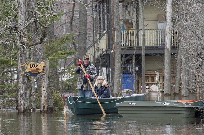 A man and woman use a boat to move along a street in the town of Rigaud, Que., west of Montreal, Thursday, April 20, 2017, following flooding in the area.