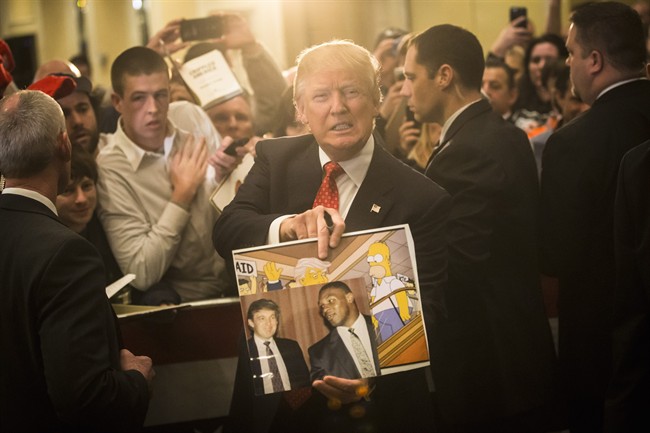 In this Jan. 29, 2016, file photo, Republican presidential candidate Donald Trump holds depictions of himself on, "The Simpsons" and a photo with boxer Mike Tyson, given to him by an attendee during a campaign stop at the Radisson Hotel in Nashua, N.H.