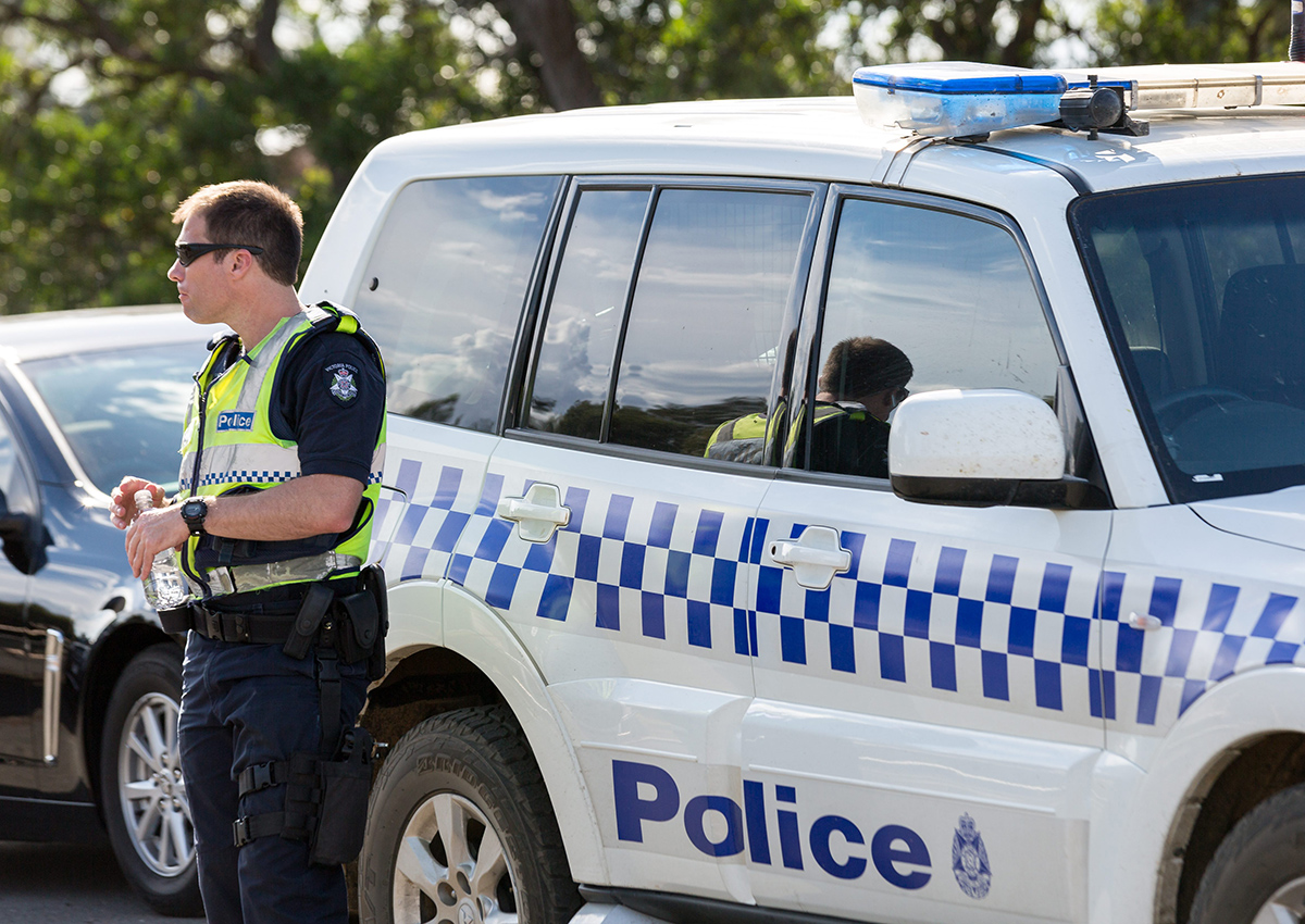 A policeman standing near a police car in Australia. Four people have been arrested in Australia after more than $155-million AUD ($140-million CAD) worth of illegal drugs were discovered in a vintage car shipped from Canada.