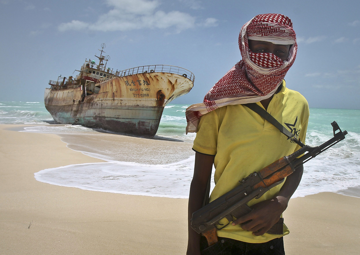  In this Sunday, Sept. 23, 2012 file photo, masked Somali pirate Hassan stands near a Taiwanese fishing vessel that washed up on shore after the pirates were paid a ransom and released the crew, in the once-bustling pirate den of Hobyo, Somalia. 