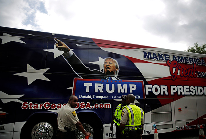Police stand watch outside the NRA annual convention where President Donald Trump is scheduled to speak later in the day as a bus promoting his 2020 re-election passes by in Atlanta, Friday, April 28, 2017. 