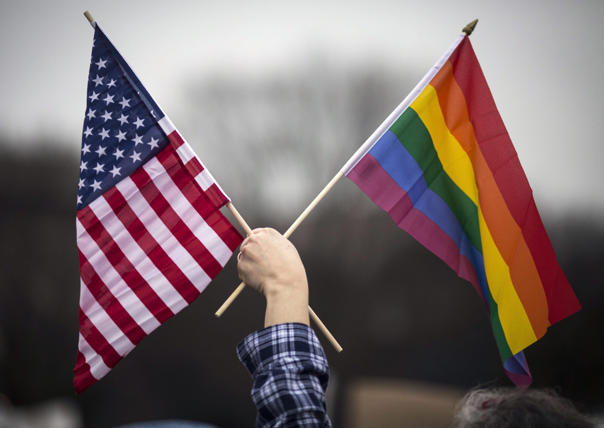 A participant holds both the U.S. national flag (L) and the LGBT community's symbolic  Rainbow flag (R) as people arrive on the mall for the Million Woman March in Washington in January. 