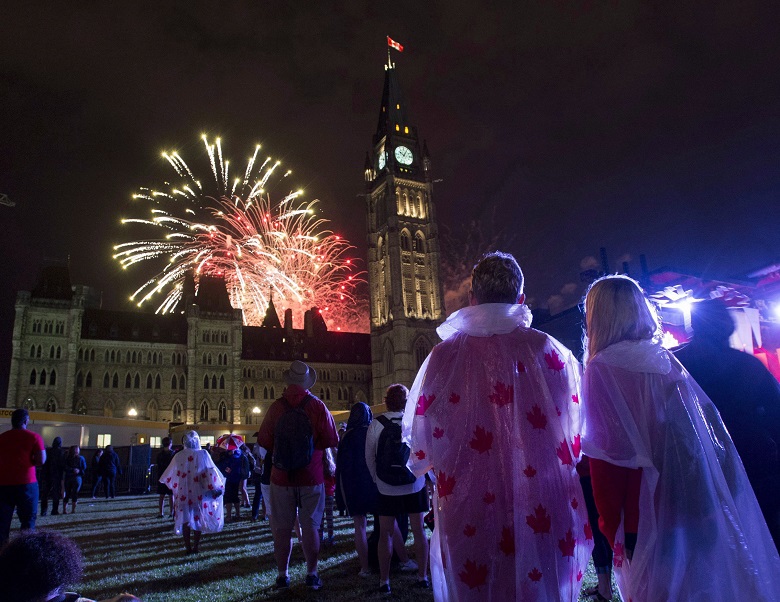 People watch fireworks as they explode behind the Peace Tower during Canada Day celebrations on Parliament Hill on Friday, July 1, 2016 in Ottawa. 