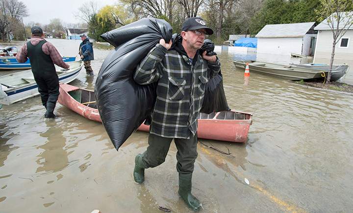 A man carries bags out of a canoe at the edge of the floodwaters Sunday May 7, 2017 in Gatineau, Que.