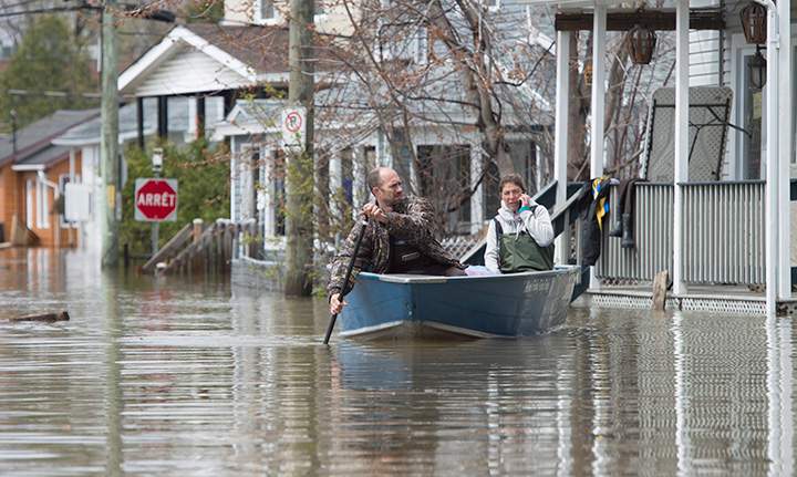 A woman speaks on a phone as a man guides their boat through the floodwaters, Sunday May 7, 2017 in Gatineau, Que.