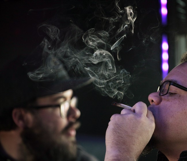 Phoenix Camacho, of Austin, Texas, right, smokes a marijuana cigarette as Scott Craft, of Aurora, Colo., looks out the window of a tour bus on Wednesday, April 26, 2017 throughout Denver.