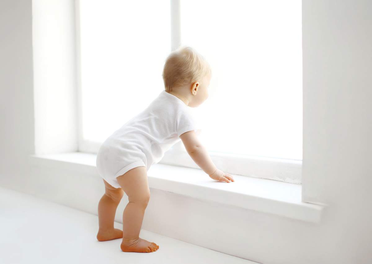 FILE: Baby stands near window.
