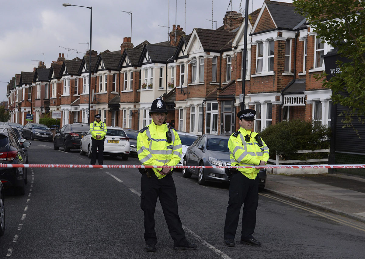 In this picture taken Friday, April 28, 2017, police officers man the cordoned off area in London's Harlesden Road after British counter-terror police have shot a woman and arrested several people in raids in London and southeastern England.