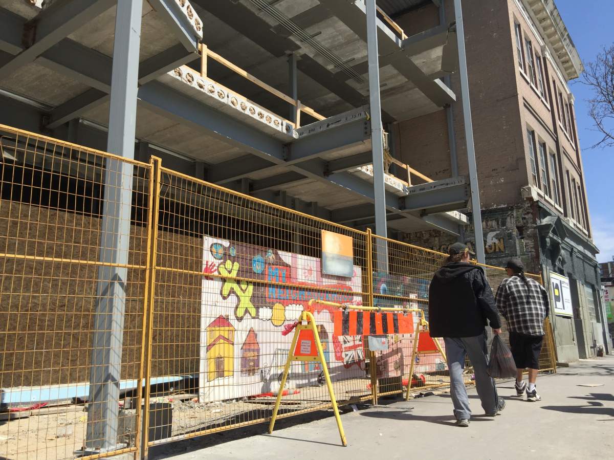 A metal fence separates the empty building from people walking by on Selkirk Avenue.