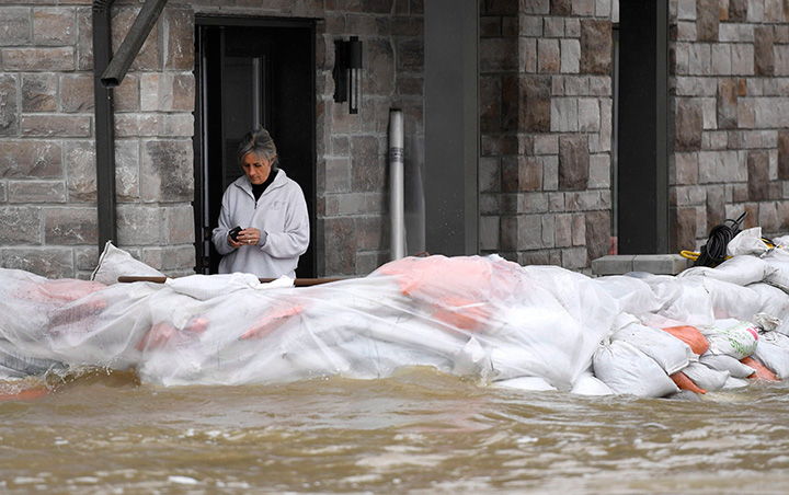 A resident uses her phone from behind sandbags at the front of a home on Voisine Road in Rockland, Ont., about 40 kilometres east of Ottawa, on Sunday, May 7, 2017. 
