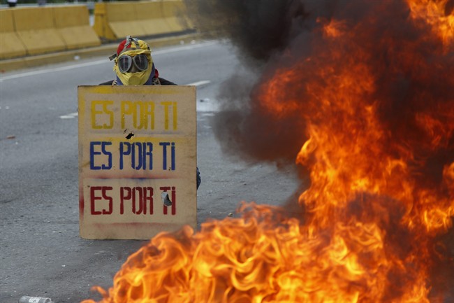 A demonstrator hols a sign that doubles a shield that reads in Spanish "It's for you," during a national sit-in against President Nicolas Maduro, in Caracas, Venezuela, Monday, May 15, 2017.