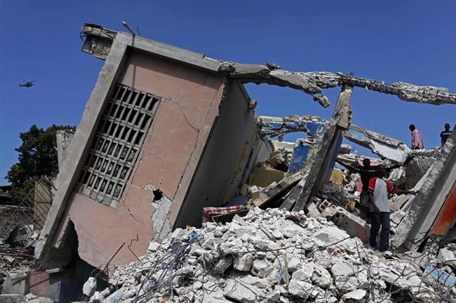 FILE - In this Jan. 30, 2010, file photo, people stand in the rubble of a collapsed building in the aftermath of a massive earthquake in Port-au-Prince.