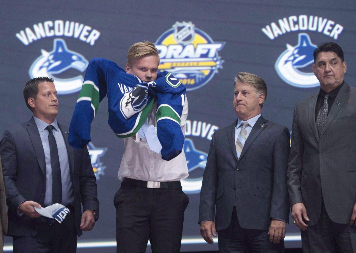 Olli Juolevi, fifth overall pick, puts on his sweater as he stands on stage with members of the Vancouver Canucks management team at the NHL draft in Buffalo, N.Y., on June 24, 2016. The Vancouver Canucks have signed defenceman Olli Juolevi to a three-year entry level contract.The Canucks selected Juolevi fifth overall in the 2016 draft, making him one of three Finns to go in the top five. THE CANADIAN PRESS/Nathan Denette.