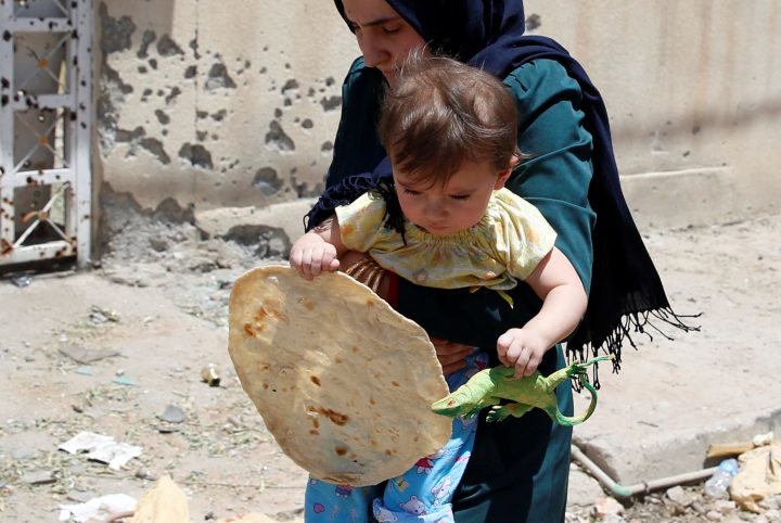 A child holds bread as she is carried by her mother who fled home due to fighting between Iraqi forces and Islamic State militants, near the Old City in western Mosul, Iraq.