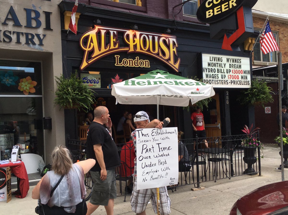 A protestor holds his own sign, below a newly posted argument against minimum wage above the Ale House's front doors on June 19th, 2017.