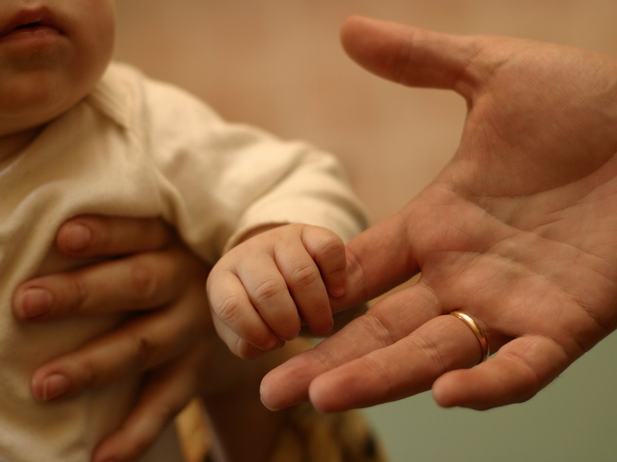 A baby holds an adult's hand.