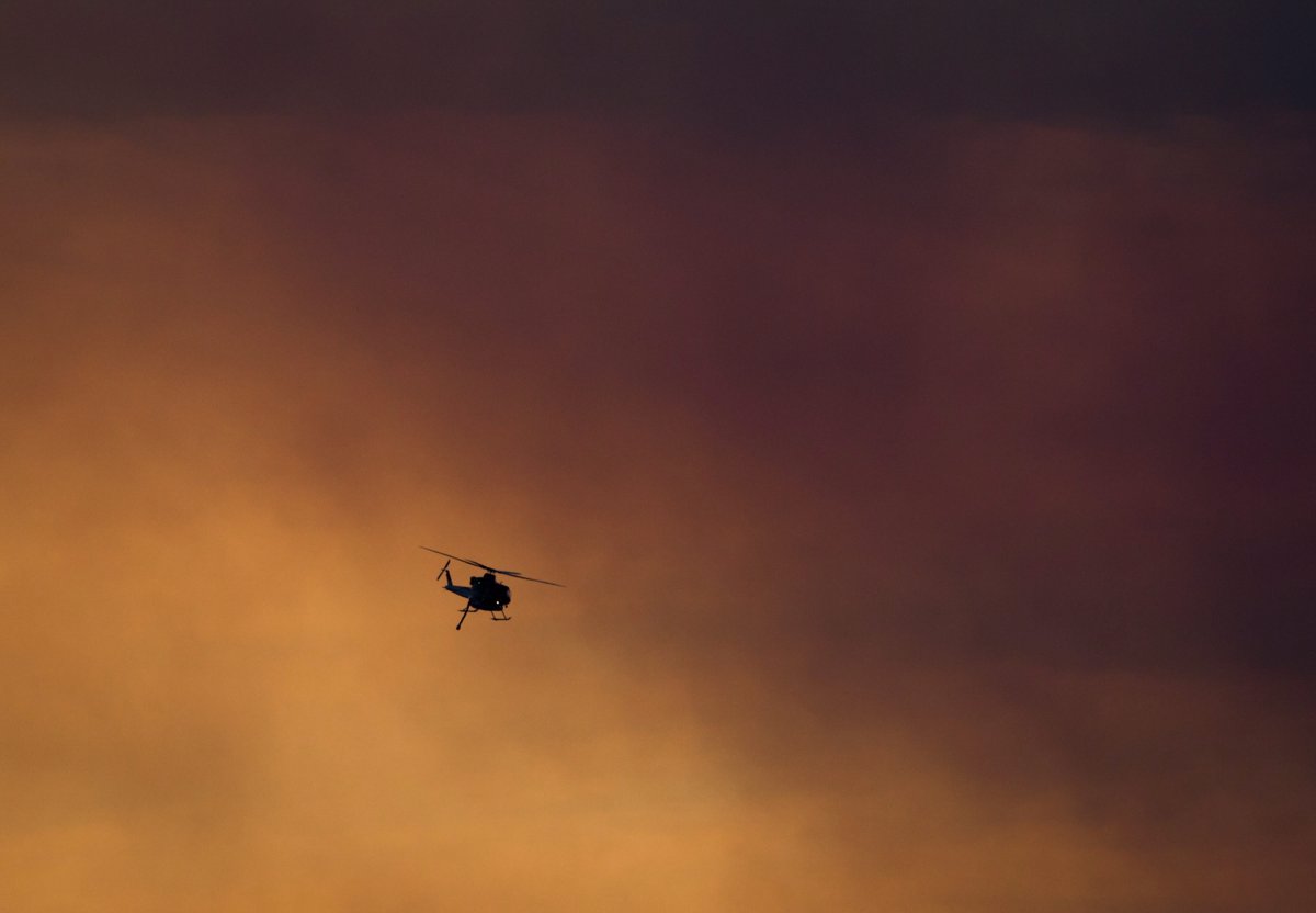 A firefighting helicopter flies past smoke in the air from a wildfire burning near Ashcroft, B.C., at sunset on Friday July 7, 2017. 
