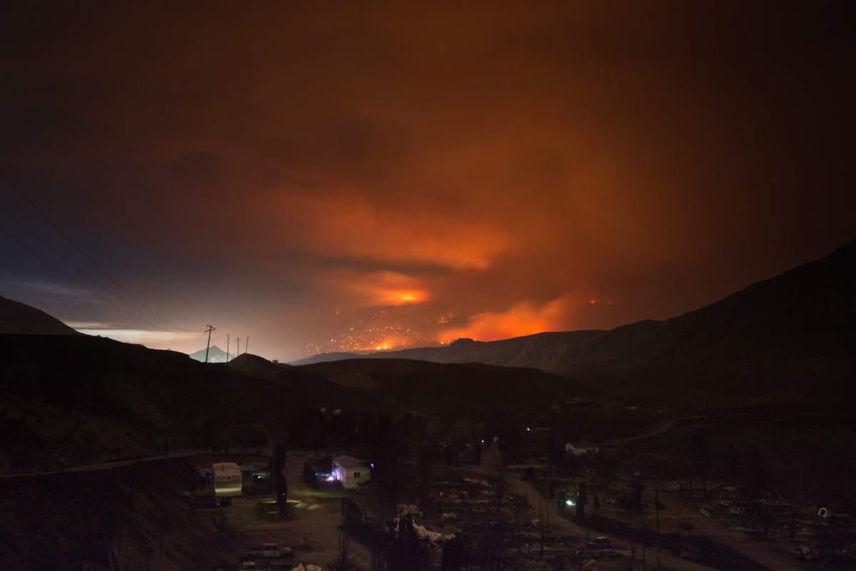 A wildfire burns on a mountain in the distance east of Cache Creek behind a trailer park that was almost completely destroyed by wildfire, in Boston Flats, B.C., in the early morning hours of Monday July 10, 2017. 