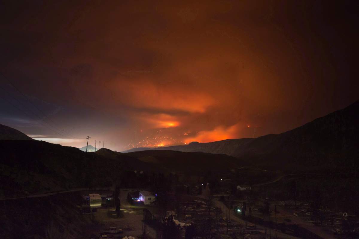 A wildfire burns on a mountain in the distance east of Cache Creek behind a trailer park that was almost completely destroyed by wildfire, in Boston Flats, B.C., in the early morning hours of July 10, 2017. THE CANADIAN PRESS/Darryl Dyck