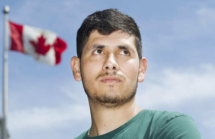 A Canadian flag flaps in the wind behind migrant worker Henry Aguirre of Guatemala during a demonstration in Montreal, Sunday, July 23, 2017.