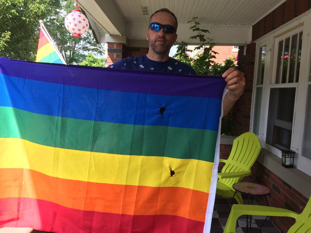 Brad Schweitzer holds up the pride flag, which he discovered folded on his porch with cigarette burns. 