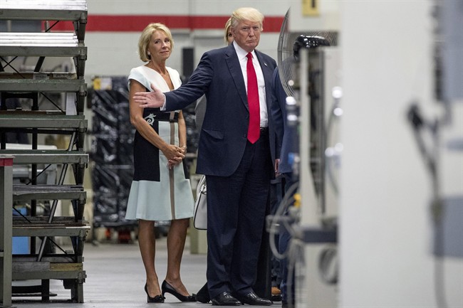 In this June 13, 2017, file photo, President Donald Trump, accompanied by Education Secretary Betsy DeVos, left, waves to members of the media as he takes a tour of Waukesha County Technical College in Pewaukee, Wis.