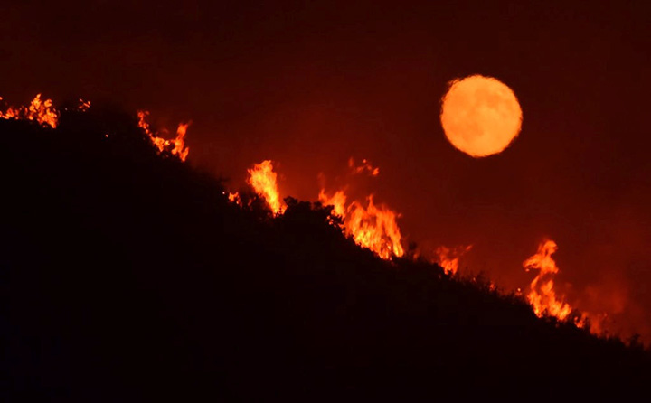 The full moon rises over flames of the Alamo fire on a hilltop east of Santa Maria, California on July 7, 2017.