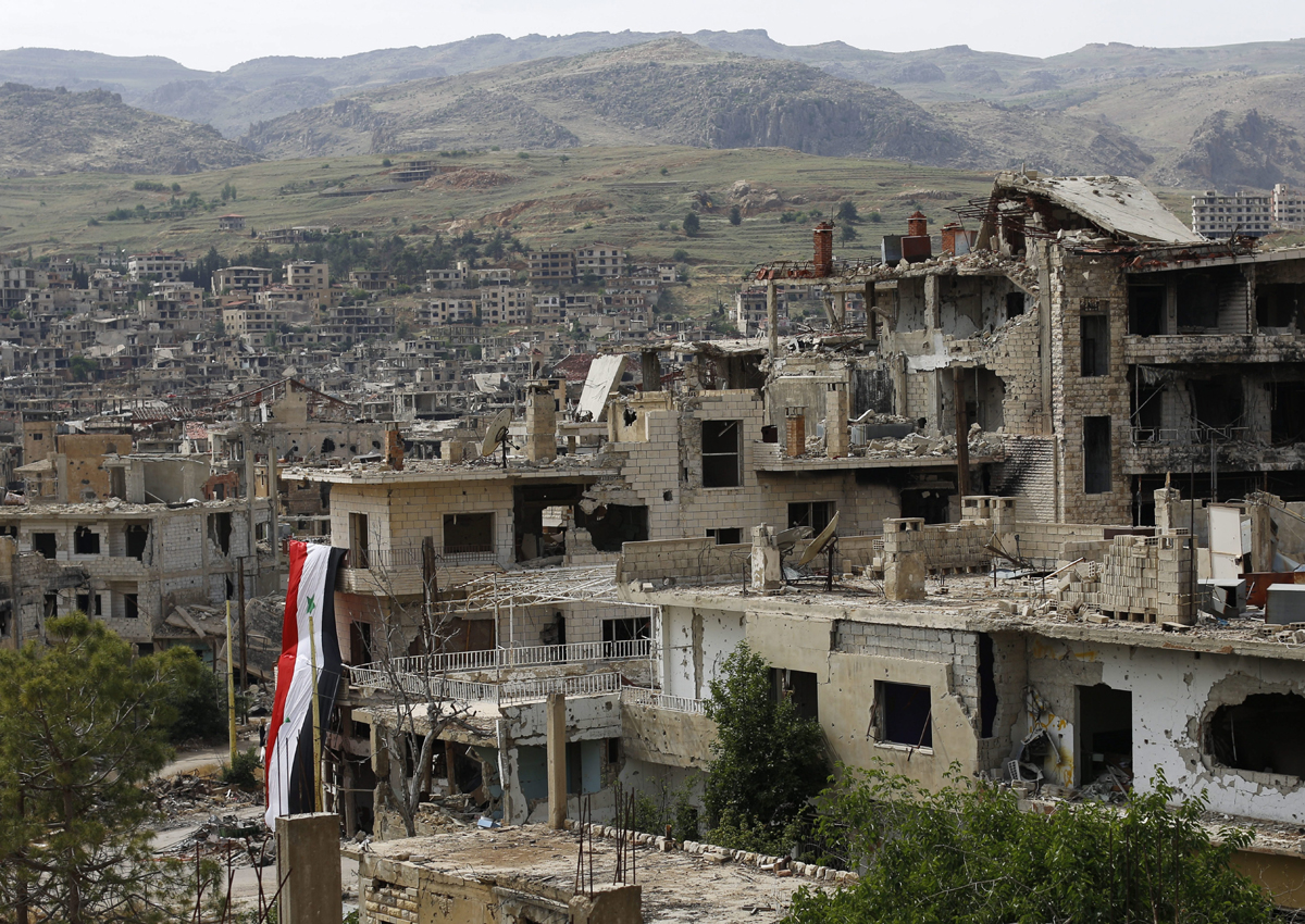 In this May 18, 2017 file photo, a Syrian National flag hangs out of a damaged building at the mountain resort town of Zabadani in the Damascus countryside, Syria. 