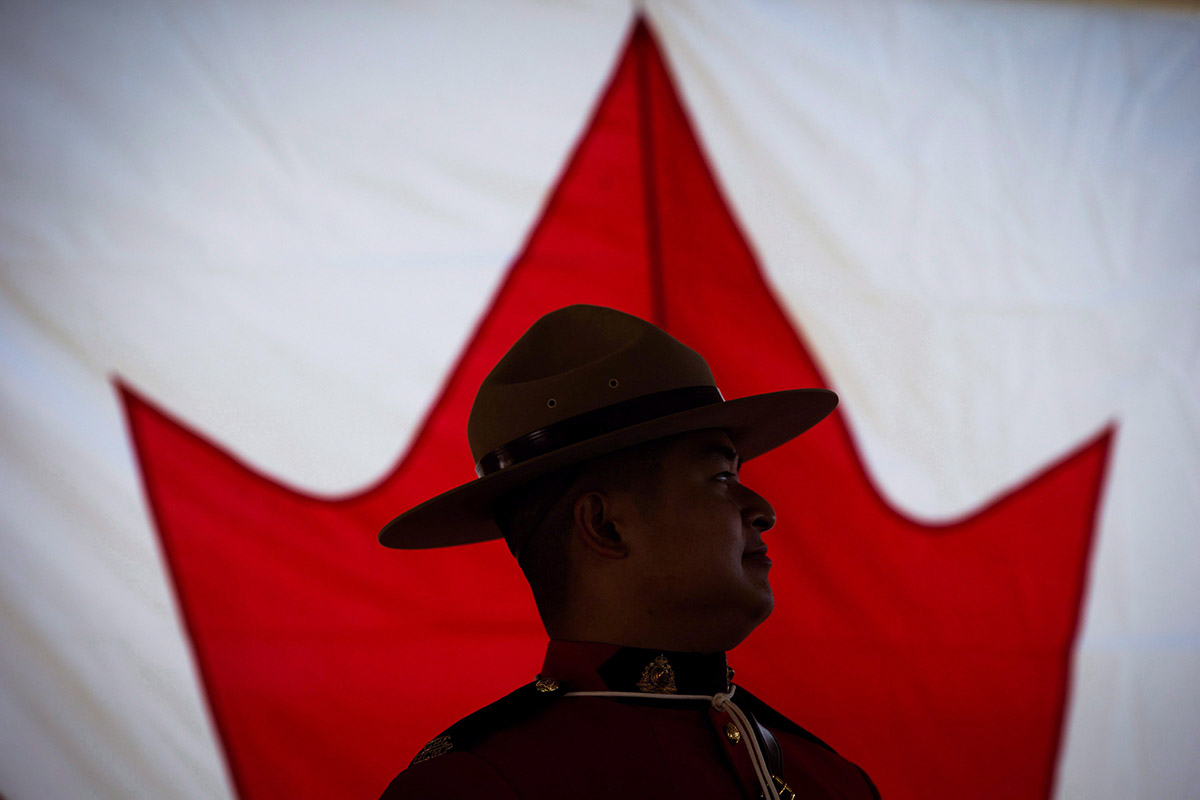 An RCMP officer is silhouetted against a Canadian flag during a special Canada Day citizenship ceremony in West Vancouver, B.C., on Saturday, July 1, 2017. 