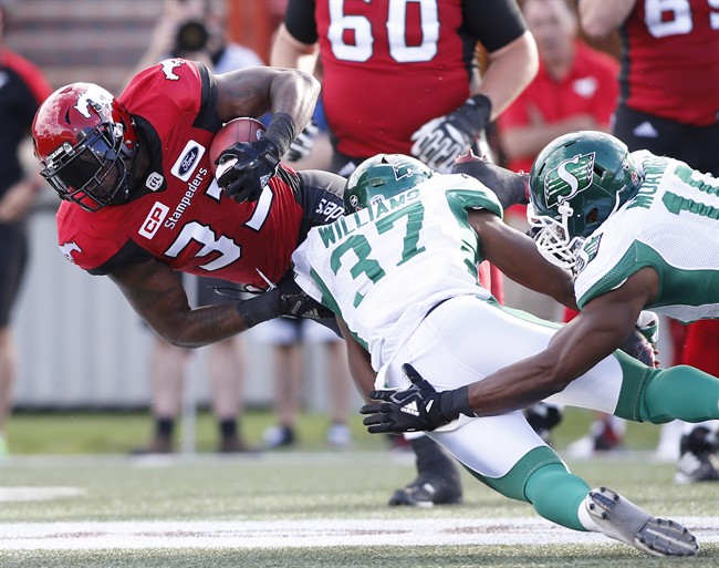 Calgary Stampeders' Jerome Messam, left, muscles past Saskatchewan Roughriders' Sam Williams, centre, and Henoc Muamba during first half CFL football action in Calgary, Ab. on Saturday July 22, 2017.