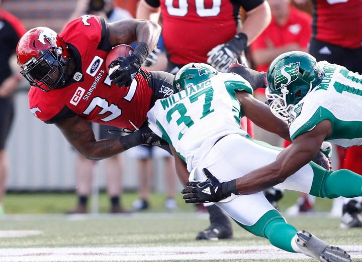 Calgary Stampeders' Jerome Messam, left, muscles past Saskatchewan Roughriders' Sam Williams, centre, and Henoc Muamba during first half CFL football action in Calgary on Saturday.