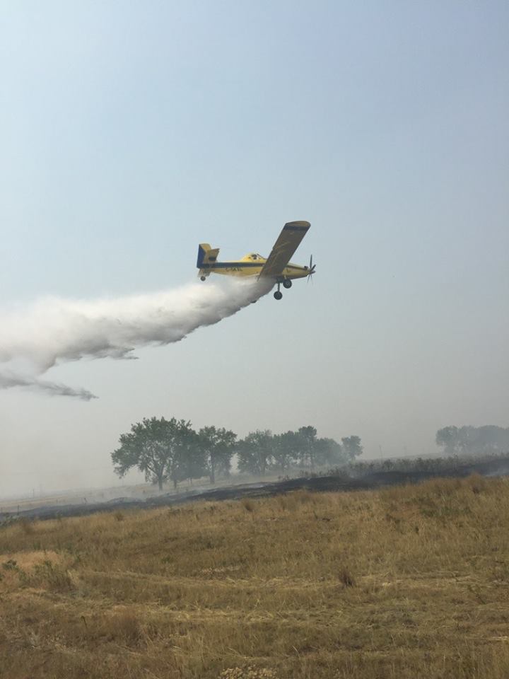 A spray plane assists fire crews near Taber extinguish a grass fire