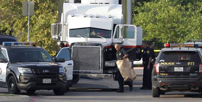 San Antonio police officers investigate the scene where eight people were found dead in a tractor-trailer loaded with at least 30 others outside a Walmart store in stifling summer heat.