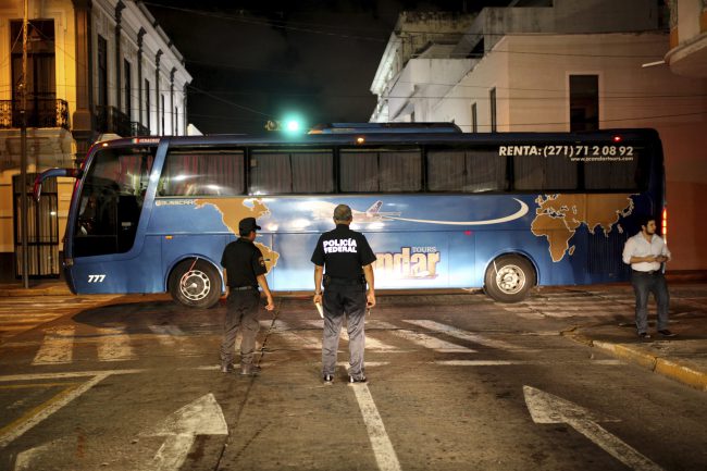 Police watch the departure of a private bus used by Mexican authorities to transport Central American migrants to a migrant detention facility in Veracruz, Mexico, Aug. 19, 2017.